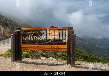 Skagway, Alaska, USA - 20 luglio 2011: Autostrada Klondike per il Canada. Colorato cartello di benvenuto vicino al confine. Nuvolosità nella parte posteriore. Foto Stock