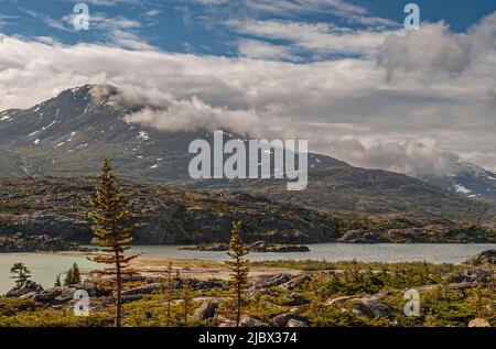 Skagway, Alaska, USA - 20 luglio 2011: Autostrada Klondike per il Canada. Nuvoloso paesaggio sulle Montagne Rocciose canadesi con le zone innevate e Summer Lake in fondo. Foto Stock