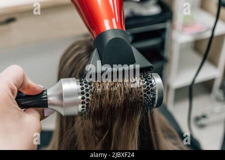 Il parrucchiere asciuga i capelli lunghi e marroni con una spazzola rotonda. Foto di alta qualità Foto Stock