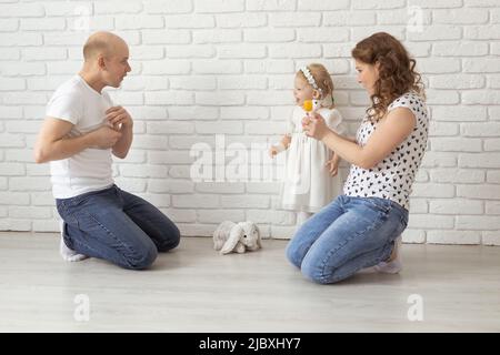 Il bambino con gli apparecchi acustici e gli impianti cocleari gioca con i genitori sul pavimento. Concetto di sordi e riabilitazione e diversità Foto Stock