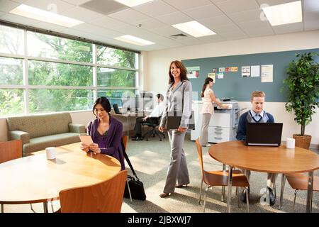 Ritratto di una donna d'affari sicura in piedi in ufficio con i suoi moli che lavorano intorno a lei. Foto Stock