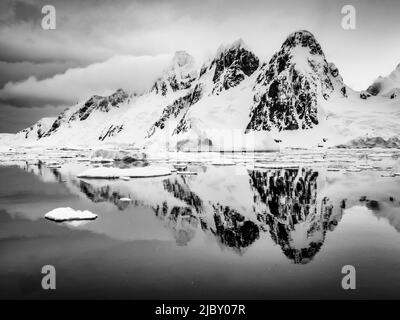 Bianco e nero, il ghiaccio del pacchetto forma le piscine riflettenti per la costa montagnosa di Booth Island, Antartide Foto Stock