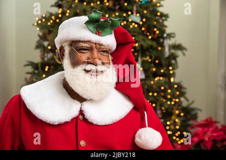 Primo piano ritratto di un uomo nero con barba bianca naturale vestita come Babbo Natale. Foto Stock