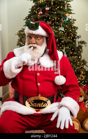 Un Babbo Natale nero che guarda la fotocamera e fa un gesto shushing. Foto Stock