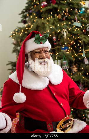 Uomo anziano vestito come Santa Nera con le braccia aperte verso la macchina fotografica sorridente. Foto Stock