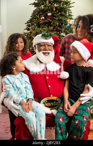Felice famiglia afroamericana tutti riuniti intorno a Babbo Natale. Black Santa Series. Foto Stock