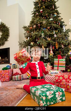 Ragazzo vestito di pigiami di stagione seduto da Natale albero di apertura doni. Foto Stock