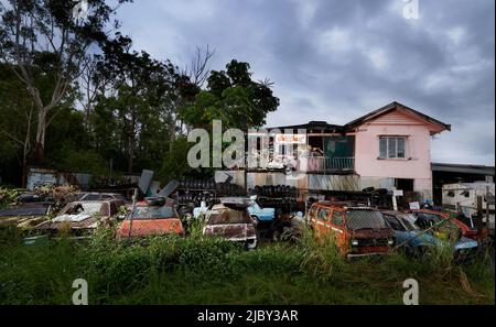 Vecchia auto che esplica dal lato della casa rosa al cantiere di relitto auto Foto Stock