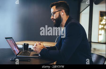 Uomo d'affari moderno che partecipa a una riunione virtuale su un laptop. Giovane imprenditore che indossa le cuffie durante una videochiamata in ufficio. uomini d'affari Foto Stock