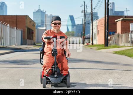 Ritratto di nano maschile in strada in Texas a bordo di uno scooter per la mobilità, fumare una sigaretta Foto Stock