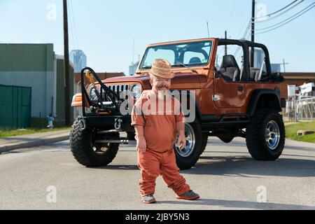 Ritratto completo di caucasico maschio adulto nana (piccola persona) in piedi in strada con un veicolo fuoristrada parcheggiato dietro di lui. Foto Stock