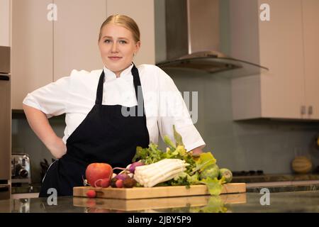 Ritratto basso angolo dello Chef Megan Gill in cucina a casa guardando la macchina fotografica con la mano sul suo fianco Foto Stock