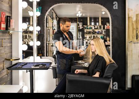 Stilista che taglia i capelli della giovane donna al salone boutique Foto Stock