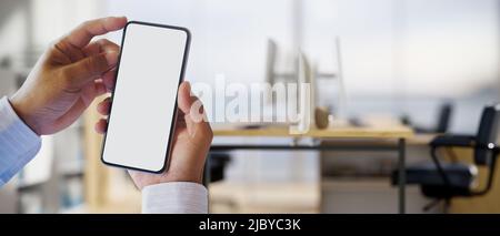 Immagine ravvicinata, Un uomo d'affari tiene uno smartphone cellulare bianco schermo mockup su ufficio sfocato sullo sfondo. 3d rendering, 3d illustri Foto Stock
