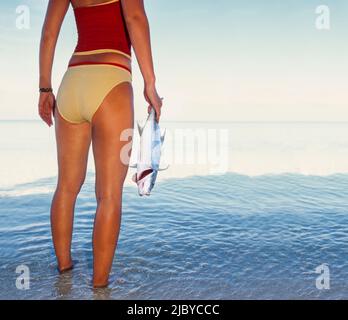 Giovane donna che indossa due costume da bagno in piedi in acqua tropicale tenendo pesci Foto Stock