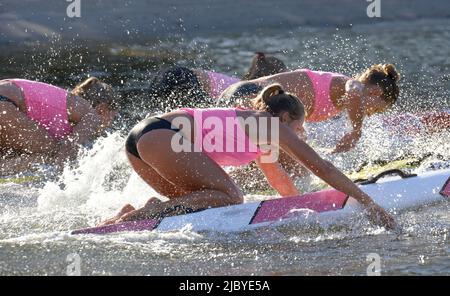 Vista laterale del team di bagnini surf femminile e paddling piatto su tavole Foto Stock