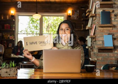 Ritratto di giovane donna seduta a tavola in libreria caffetteria con computer portatile , tenendo a mano segno fatto che legge ÒI hanno abilità Foto Stock