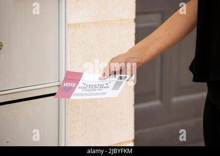 Donna che mette la posta ufficiale delle elezioni in scrutinio nella mail in uscita nel suo edificio di appartamento Foto Stock