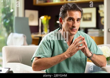 Ritratto di ispanico medico maschile seduto nel suo ufficio di casa, prendendo una pausa dalla pratica di Tele-medicina Foto Stock