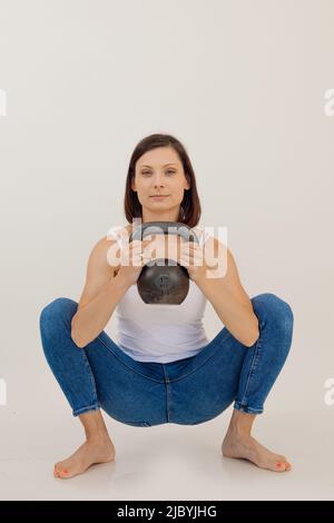 Ritratto di giovane donna sottile e sportivo, cute e muscolosa, con capelli scuri che si schiaccano su prosciutti, tenendo la campana del bollitore con le mani. Foto Stock