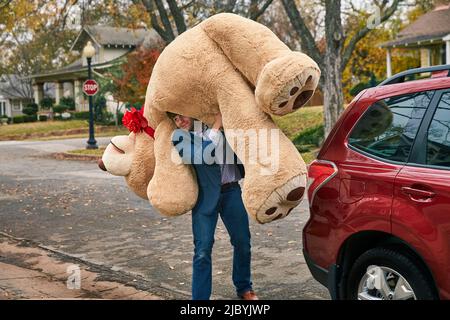 Ampio colpo di un uomo che porta un grosso orsacchiotto sopra la spalla. Foto Stock