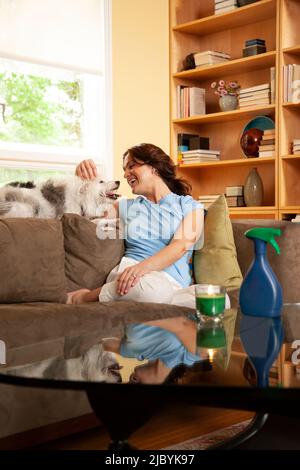 Donna a casa sul divano accarezzando il suo cane che si trova sul retro del divano Foto Stock