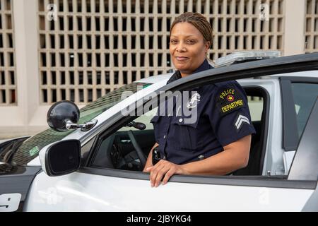 Poliziotto in piedi alla porta della macchina di polizia guardando verso la macchina fotografica sorridente Foto Stock