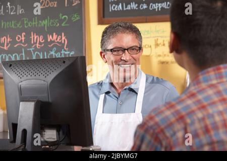 Proprietario Cafe che serve il cliente Foto Stock