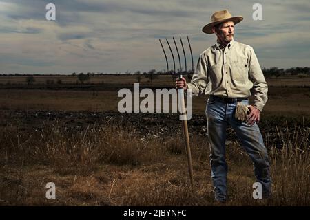 Agricoltore in piedi con forcone nel campo Foto Stock