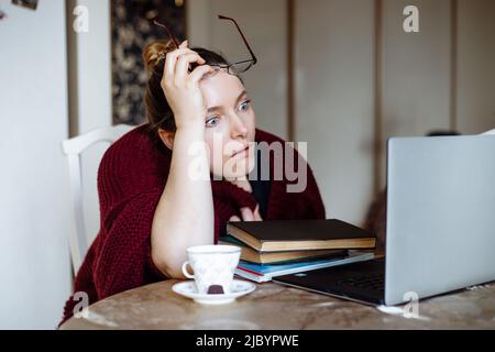 Ritratto di mezza età scioccato donna seduta a tavola a casa, guardando il laptop, tenendo gli occhiali sopra la testa in mano. Foto Stock