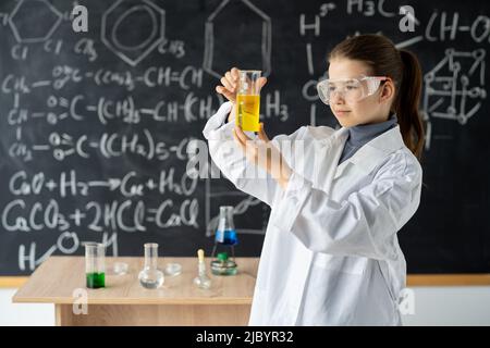 ragazza studente bambino di apprendimento ricerca e facendo un esperimento chimico mentre si fa l'analisi e la miscelazione di liquido in vetro in classe. Istruzione e. Foto Stock