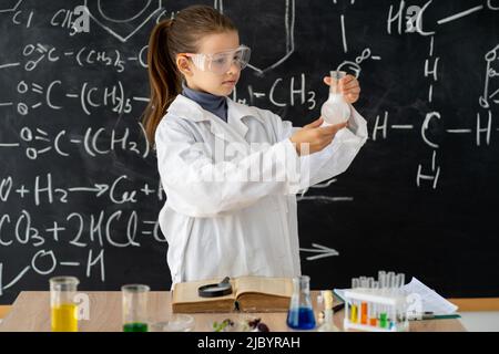 studentessa in cappotto bianco facendo esperimenti con liquidi in laboratorio di chimica, ragazza fa un esperimento chimico in una lezione di chimica Foto Stock