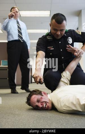 Funzionario di polizia holding battuto l uomo d affari sul pavimento in office Foto Stock