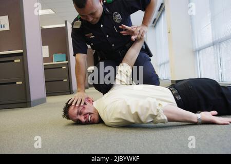 Funzionario di polizia holding battuto l uomo d affari sul pavimento in office Foto Stock