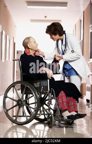 Infermiere parlando di un uomo anziano in una sedia a rotelle Foto Stock