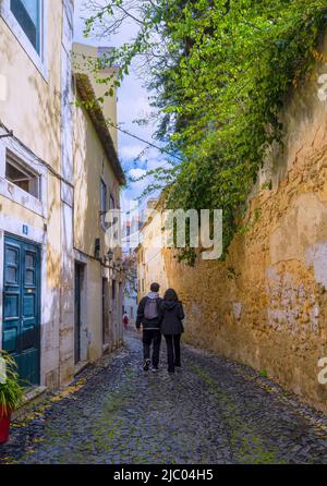 Un giovane uomo e una donna camminano lungo una stradina acciottolata nel centro di Lisbona, capitale del Portogallo Foto Stock