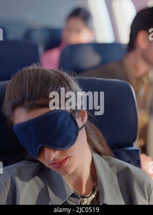 Giovane donna che dorme in aereo con la maschera per gli occhi Foto Stock