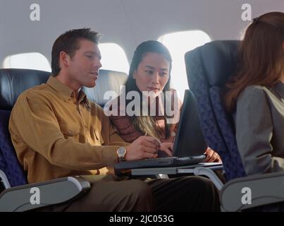 Giovane donna e uomo utilizzando laptop in aereo Foto Stock