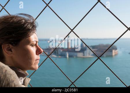 La gioia della donna la vista panoramica sull'isola di San Giorgio maggiore dietro una grata di metallo a Venezia, Veneto in Italia. Foto Stock