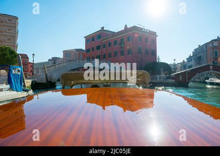 Elegante motoscafo in legno viaggia sul canale d'acqua con costruzione in un giorno di sole a Venezia, Veneto in Italia. Foto Stock