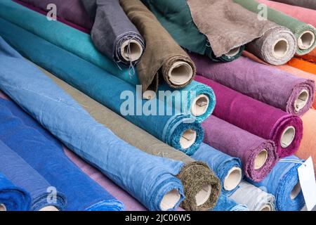 Rotoli di tessuto di lino blu e viola e fondo tessile di tela. Vecchie bobine di cartone con materiale colorato su una bancarella del mercato al dettaglio, primo piano, Foto Stock