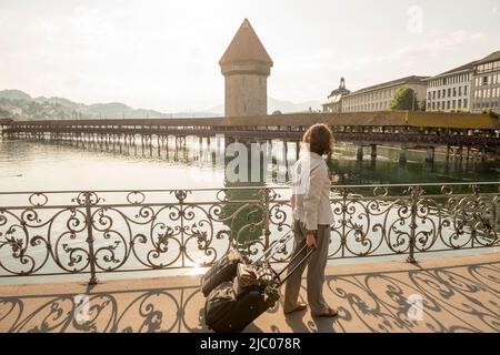 Donna con valigia che attraversa un ponte e che guarda il Ponte della Cappella con il sole a Lucerna, Svizzera. Foto Stock