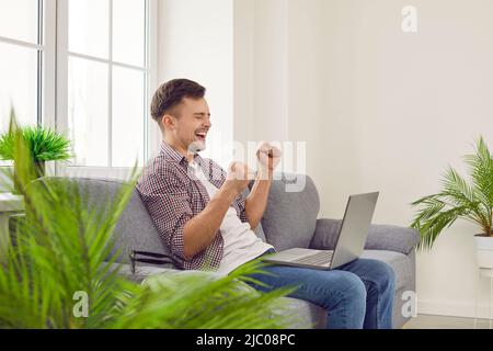 Gioiosa ragazzo eccitato con laptop gioisce in successo, vittoria, buon profitto o nuovo lavoro. Foto Stock