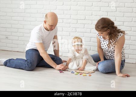 Il bambino con gli apparecchi acustici e gli impianti cocleari gioca con i genitori sul pavimento. Concetto di sordi e riabilitazione e diversità Foto Stock
