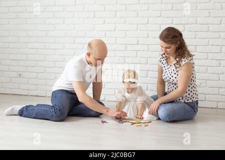 Il bambino con gli apparecchi acustici e gli impianti cocleari gioca con i genitori sul pavimento. Concetto di sordi e riabilitazione e diversità Foto Stock