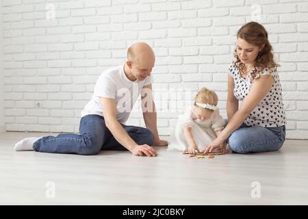 Il bambino con gli apparecchi acustici e gli impianti cocleari gioca con i genitori sul pavimento. Concetto di sordi e riabilitazione e diversità Foto Stock