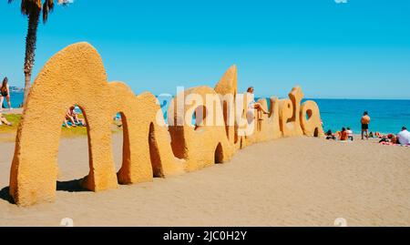 Malaga, Spagna - 26 maggio 2022: Una giovane donna sta posando per una foto seduta sul cartello popolare Malagueta alla spiaggia la Malagueta a Malaga, Spagna, in a Foto Stock