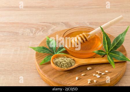 miele sano con prodotti di cannabis in una ciotola su un asse di legno rotondo. terreno e semi interi di morejuana. Vista frontale con sfondo in legno Foto Stock