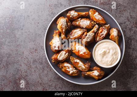 Porzione di ali di pollo alla griglia con salsa barbecue bianca Alabama da vicino in un piatto sul tavolo. Vista dall'alto orizzontale Foto Stock