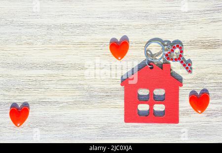 Chiave decorata con rhinestones, portachiavi a forma di casa rossa e piccoli cuori su uno sfondo di legno. Concetto di movimento romantico in Together. Foto Stock